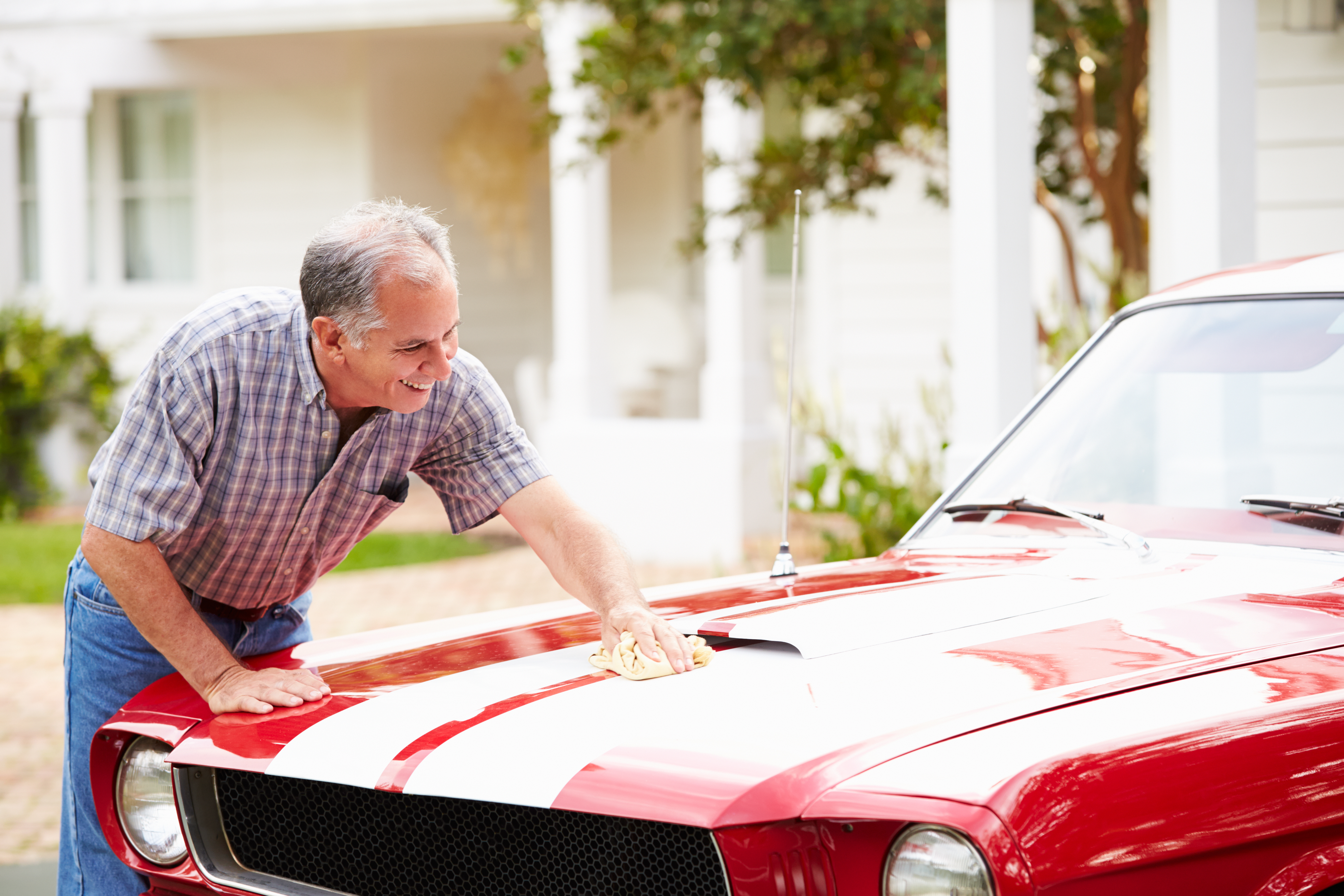 A mature man is wiping his classic car with a towel.