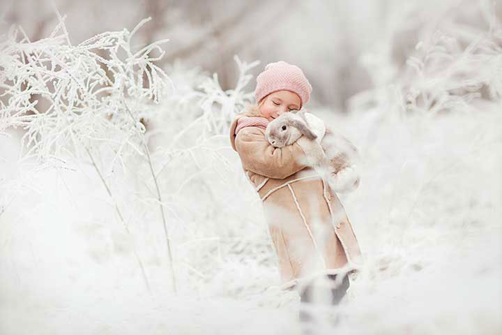 Little girl in pink hat holding a flop-earred bunny with snow in the background
