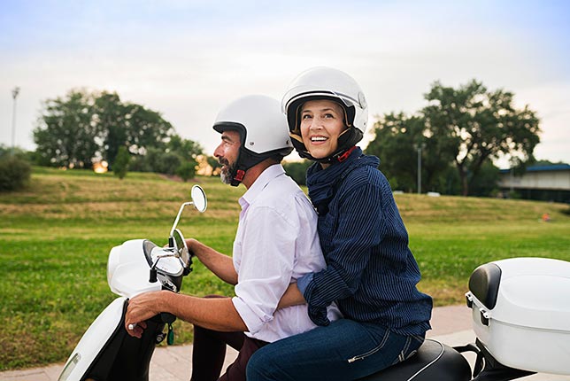 A happy couple riding in tandem on scooter