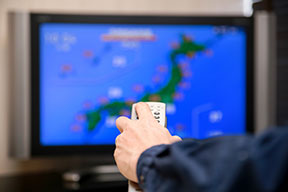 A man holding a TV remote with a weather radar map on the TV
