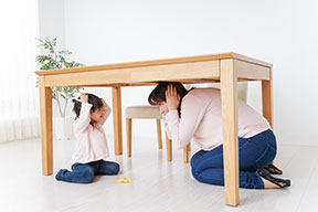 A mother and child under a sturdy table covering their heads with their hands