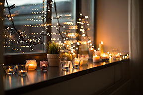 Holiday lights and an array of votive candles in front of a window