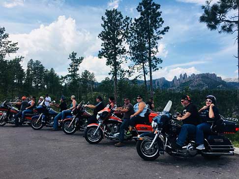 Several motorcyclists and motorcycles parked and ready to ride with the Black Hills in the background